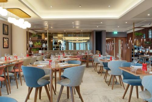 a restaurant with wooden tables and blue chairs at Hilton Garden Inn London Heathrow Terminal 2 and 3 in Hillingdon
