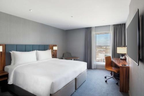 - une chambre avec un grand lit, un bureau et une fenêtre dans l'établissement Hilton Garden Inn London Heathrow Terminal 2 and 3, à Hillingdon