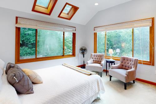 a bedroom with a bed and two chairs and windows at The Three Cornered Pond Retreat in Augusta