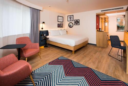 a bedroom with a bed and two chairs and a rug at Hampton by Hilton London Park Royal in London