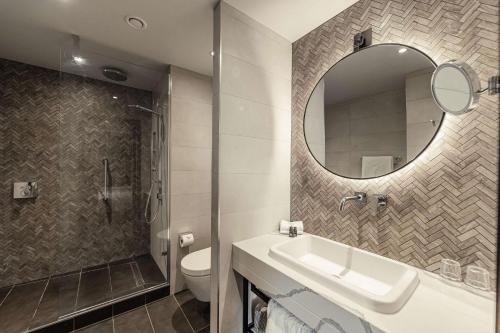 a bathroom with a sink and a mirror and a toilet at The Fellows House Cambridge, Curio Collection By Hilton in Cambridge