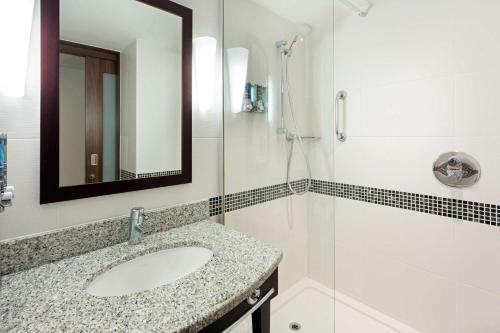 uma casa de banho com um lavatório, um chuveiro e um espelho. em Hampton by Hilton London Croydon em Croydon