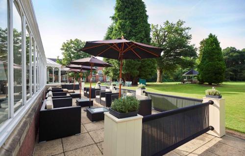 a patio with tables and chairs with an umbrella at DoubleTree by Hilton St. Anne's Manor in Bracknell