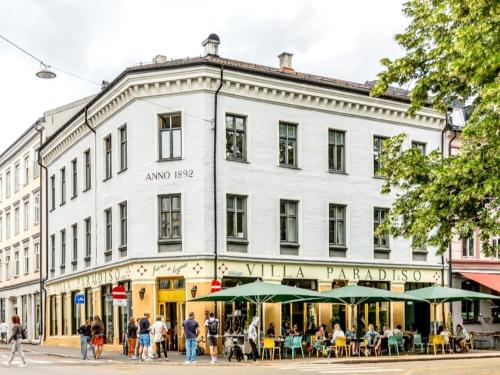a large white building with people sitting outside on a street at Modern central apartment next to beautiful nature2424 in Oslo