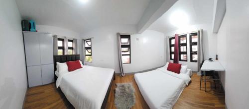 2 camas en una habitación con paredes y ventanas blancas en Lorenzo's Homestay, en Basco