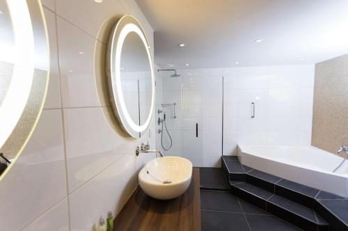 Baño blanco con lavabo y espejo en DoubleTree by Hilton Royal Parc Soestduinen en Soestduinen