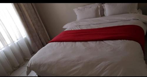 a bed with a red and white blanket and a window at Sagewood Manor in Midrand