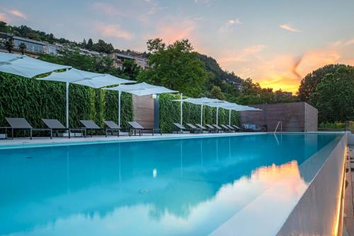 a swimming pool with white umbrellas and chairs at Hilton Lake Como in Como