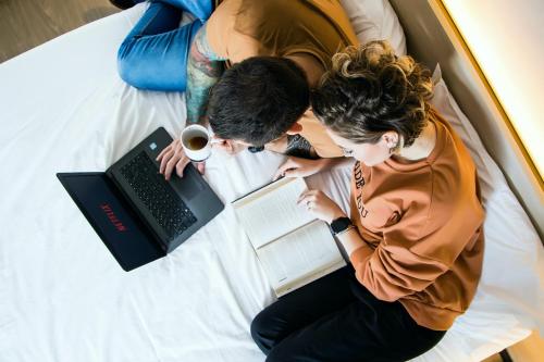 a man and woman sitting on a bed with a laptop at Naalt Hotel Joinville in Joinville