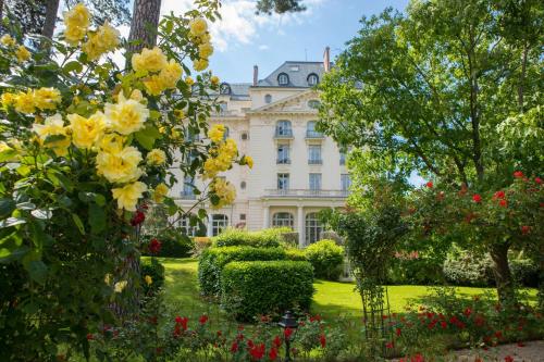 een groot wit huis met gele bloemen in de tuin bij Waldorf Astoria Versailles - Trianon Palace in Versailles