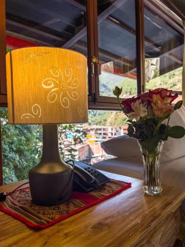a lamp on a table next to a vase of flowers at Rupa Rupa High Jungle Eco B&B in Machu Picchu