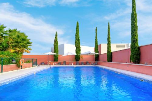 a swimming pool with trees and a building at Hilton Garden Inn Málaga in Málaga