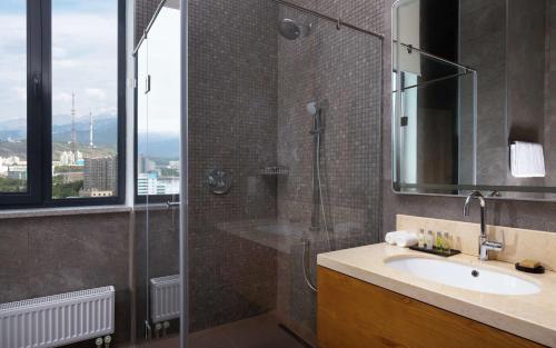 a bathroom with a shower and a sink and a mirror at DoubleTree by Hilton Almaty in Almaty