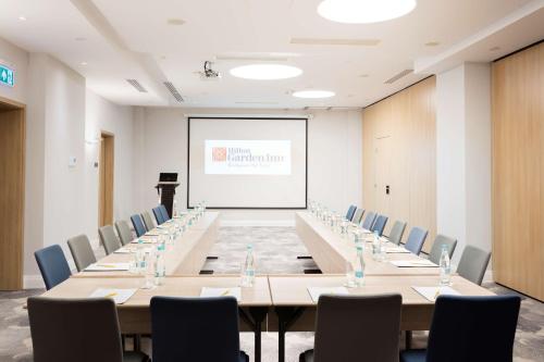 a conference room with long tables and chairs and a white screen at Hilton Garden Inn Bucharest Old Town in Bucharest