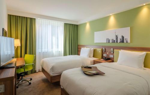 a hotel room with two beds and a desk and a television at Hampton by Hilton Frankfurt City Centre in Frankfurt