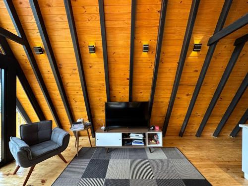 sala de estar con TV y silla en Cabanas River House Urubici - Chalé River House e Chalé Bela Vista, en Urubici