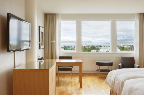 a hotel room with a desk and a bed and windows at Hilton Reykjavik Nordica in Reykjavík