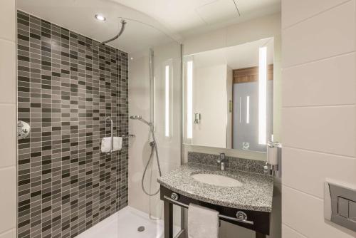 uma casa de banho com um lavatório e um chuveiro com um espelho. em Hampton By Hilton Munich City West em Munique