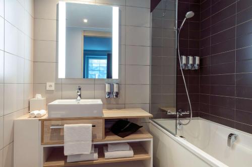 a bathroom with a sink and a mirror and a tub at Hampton By Hilton Paris Clichy in Clichy