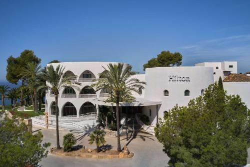 een gebouw met palmbomen ervoor bij Hilton Mallorca Galatzo in Paguera