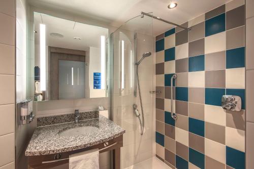 a bathroom with a sink and a shower and a mirror at Hampton by Hilton Stuttgart City Centre in Stuttgart