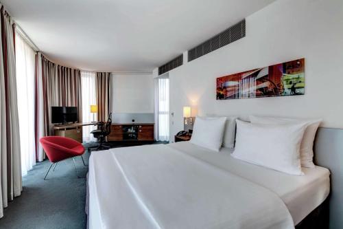 a hotel room with a white bed and a red chair at Hilton Garden Inn Stuttgart NeckarPark in Stuttgart