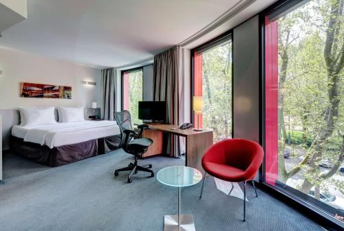 シュトゥットガルトにあるヒルトン ガーデン イン シュトゥットガルト ネッカーパークのベッド、デスク、赤い椅子が備わるホテルルームです。