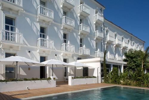 a large white building with a swimming pool and umbrellas at Grand Hotel Des Sablettes Plage, Curio Collection By Hilton in La Seyne-sur-Mer