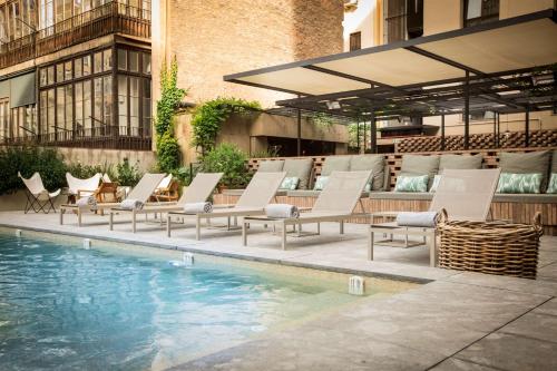 a group of lounge chairs next to a swimming pool at Alexandra Barcelona Hotel, Curio Collection by Hilton in Barcelona