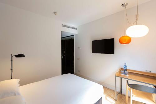 a bedroom with a bed and a desk and a tv at Alexandra Barcelona Hotel, Curio Collection by Hilton in Barcelona