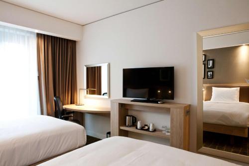 a hotel room with two beds and a desk with a television at Hampton By Hilton Dortmund Phoenix See in Dortmund