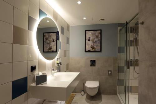 a bathroom with a sink and a toilet and a mirror at Hampton By Hilton Olsztyn in Olsztyn