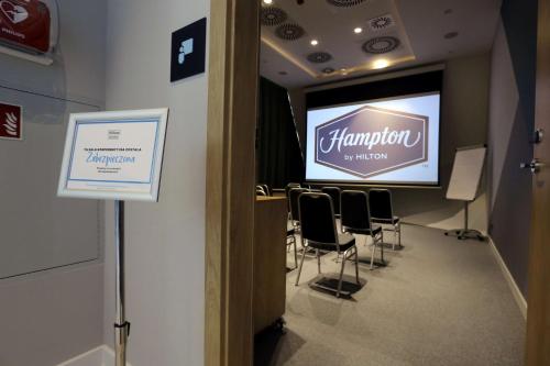 a conference room with a stage with chairs and a screen at Hampton By Hilton Olsztyn in Olsztyn