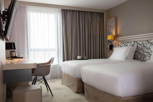 a hotel room with two beds and a desk at Hilton Garden Inn Paris Massy in Massy