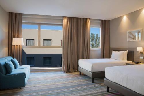 ローマにあるHampton By Hilton Rome Eastのベッド2台とソファが備わるホテルルームです。