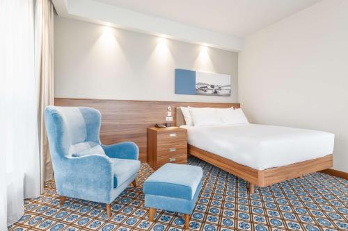 a hotel room with a bed and a blue chair at Hampton by Hilton Oswiecim in Oświęcim