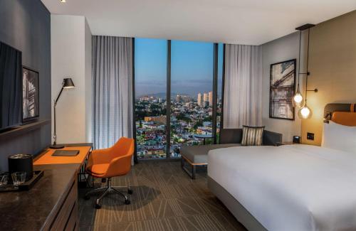 グアダラハラにあるHilton Guadalajara Midtownのベッド、デスク、ベッド、窓が備わるホテルルームです。