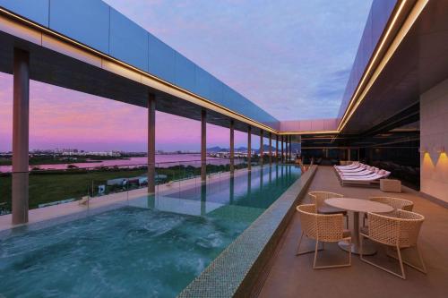 a pool on the roof of a building with tables and chairs at Hilton Barra Rio de Janeiro in Rio de Janeiro