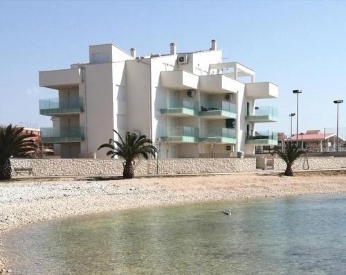 a white building with palm trees in front of a body of water at SMARAGD on the beach in Povljana