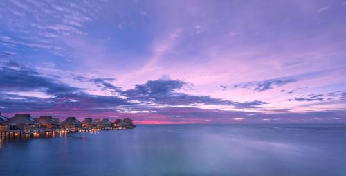 a sunset over the water with houses on a dock at Conrad Bora Bora Nui in Bora Bora