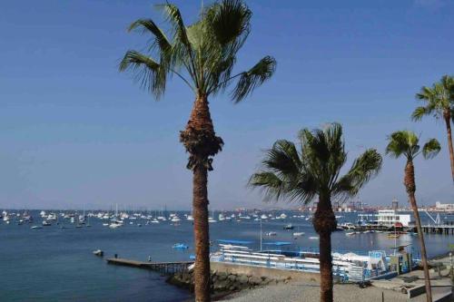 three palm trees on a beach with boats in the water at Departamento La Punta C - Piscina - Zona parrilla in Lima