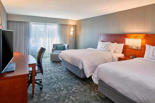 a hotel room with two beds and a desk and a television at Courtyard by Marriott Albany Thruway in Albany
