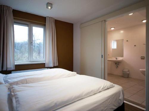 Un dormitorio con una gran cama blanca y un baño. en Villa in Texel near De Krim Holiday Park, en De Cocksdorp