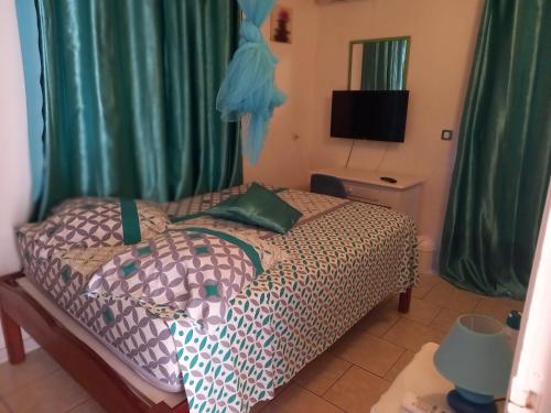 1 dormitorio con 1 cama con cortinas verdes y TV en Villa Gabève: Location F3, Bas de Villa, en Rivière-Pilote