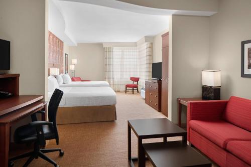 キングウッドにあるCourtyard By Marriott Houston Kingwoodのベッドと赤いソファが備わるホテルルームです。
