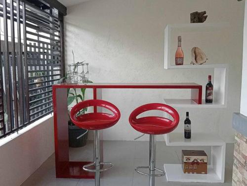 Home in San Pablo city, Laguna في سان بابلو: كرسيين حمر في بار مع زجاجات النبيذ