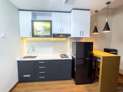 La cuisine est équipée de placards blancs et d'un réfrigérateur noir. dans l'établissement 2 kamar Amarta apartemen By Tempattinggaljog, à Kejayan