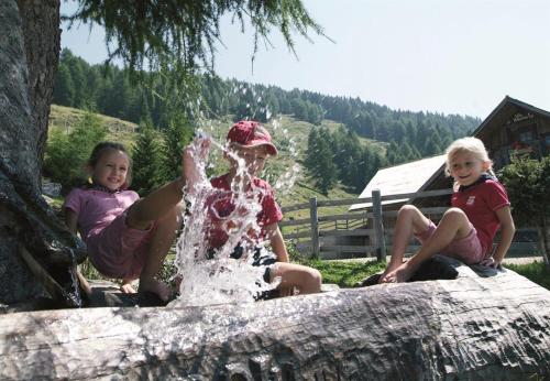 three children sitting on a log playing with a fountain at Familienhotel Steindl in Millstatt