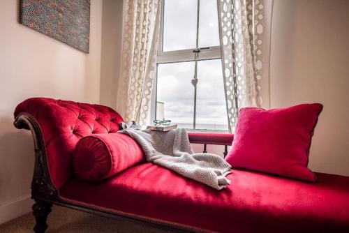 a red couch with red pillows and a window at Spindrift in Felixstowe