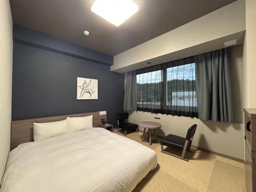 a bedroom with a bed and a table and a window at Hotel Route Inn Grand Chichibu in Chichibu